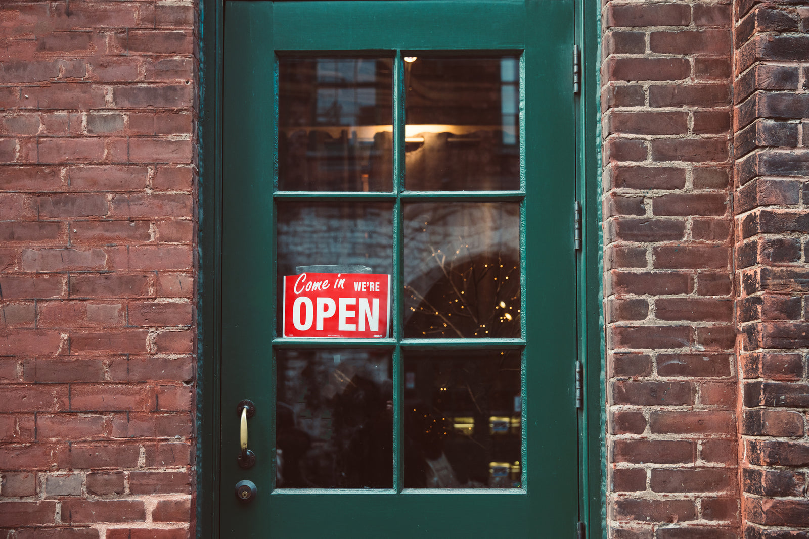 Green painted door with windows and We're Open sign welcoming customers