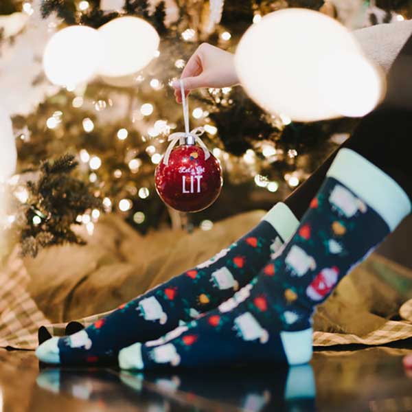 Let's Get Lit Holiday Socks and Ornament girl holding ornament wearing socks
