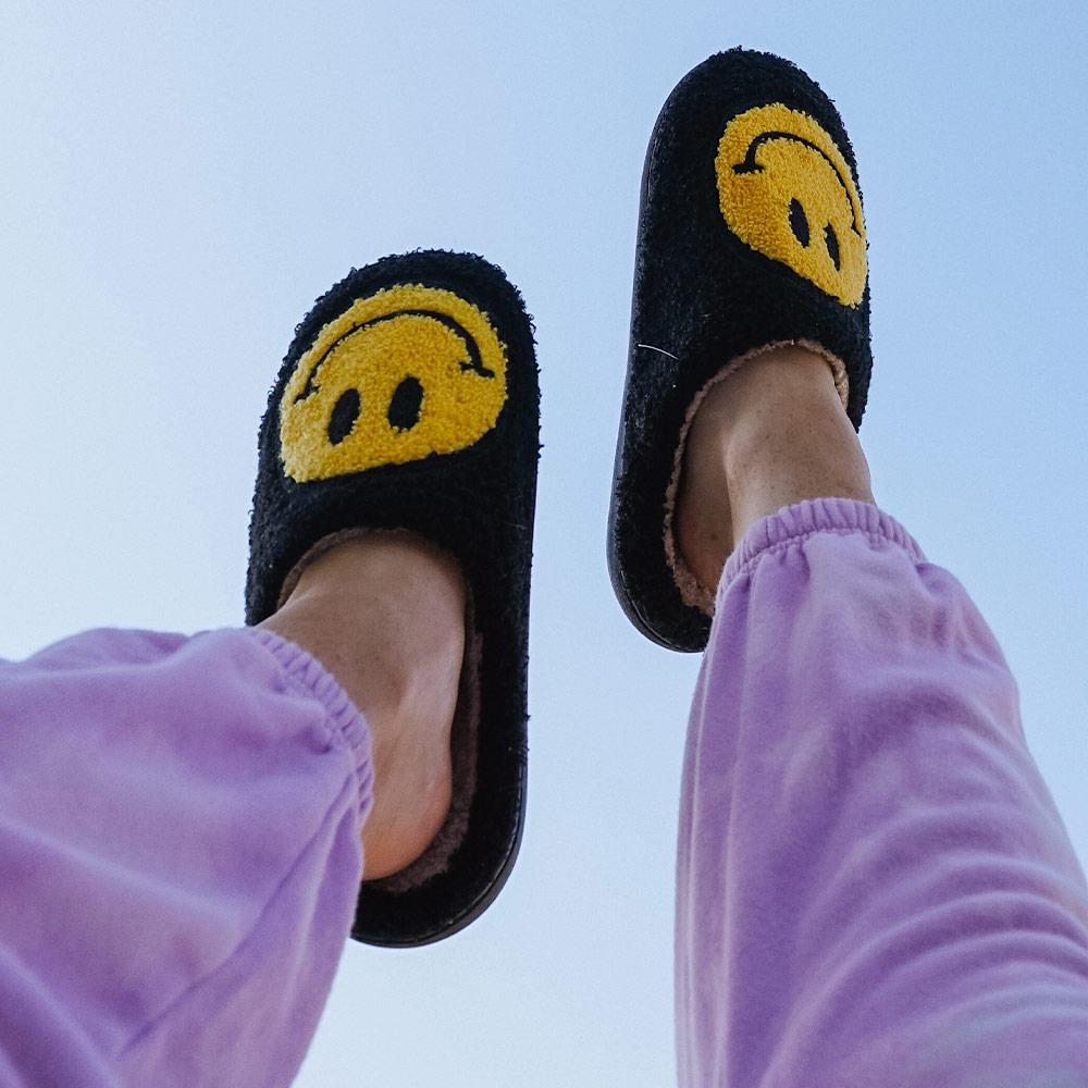 Black Fuzzy Happy Face Slippers worn by model with feet in air