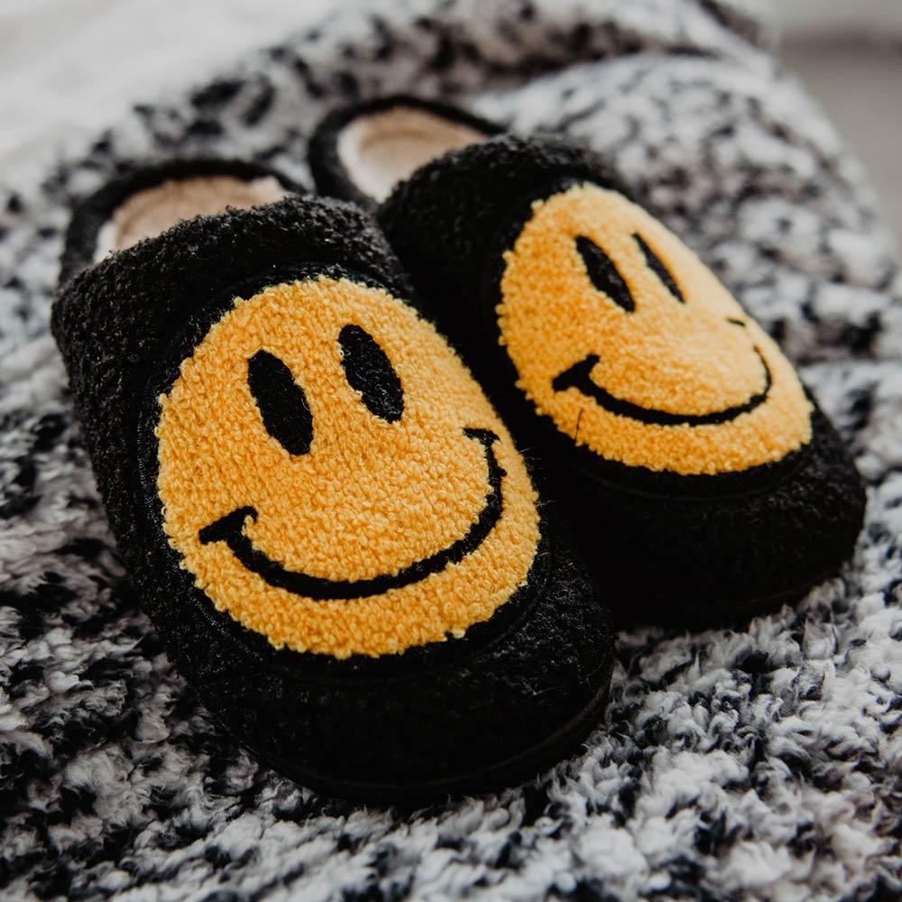 Black Fuzzy Happy Face Slippers displayed on rug