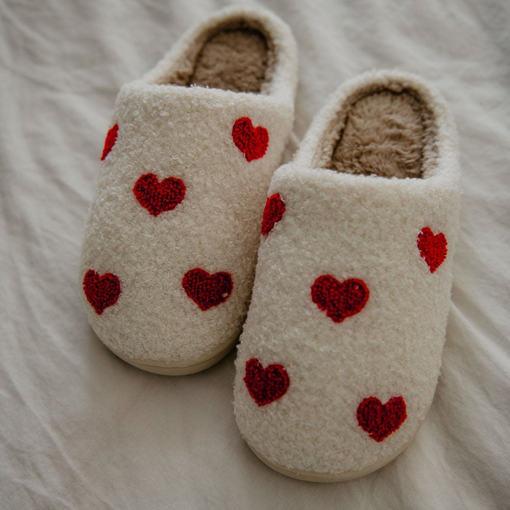 Repeat Red Heart Slippers from Katydid have small red hearts on white Sherpa material with comfy rubber soles.